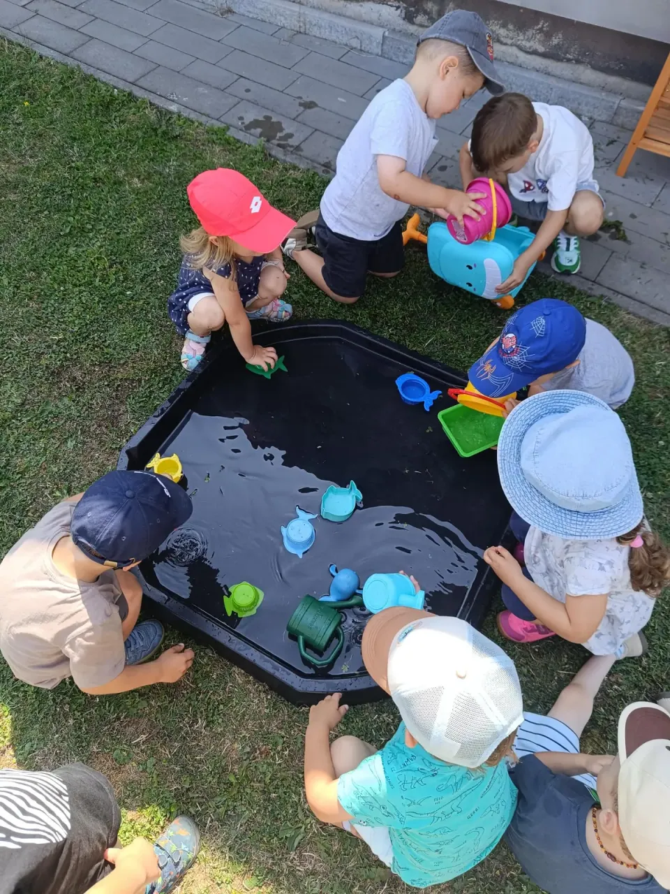 Deti sa hrajú s vodou a farebnými nádobami vonku